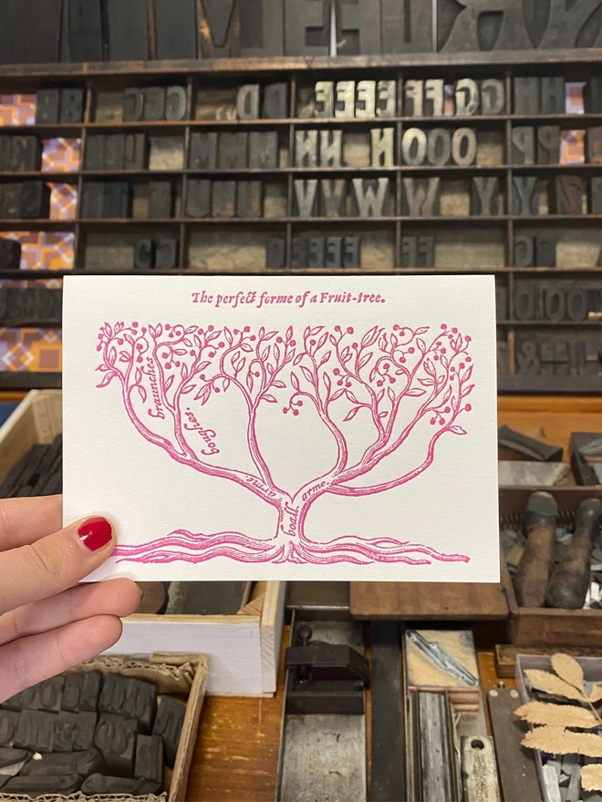 Hand holds up white greeting card with a printed pink illustration and text.