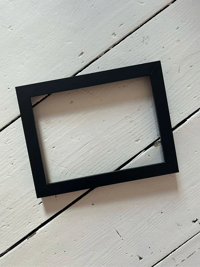 a plain black frame on a white floorboard background