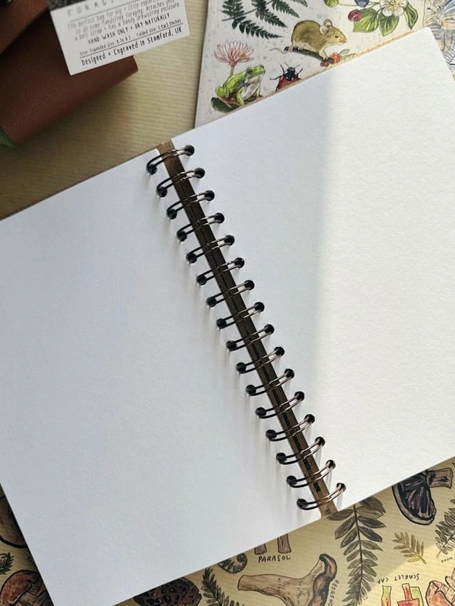 Wooden Hardback Adventure Journal, an adventure journal sitting against a colourful backdrop opened on a double page spread. 