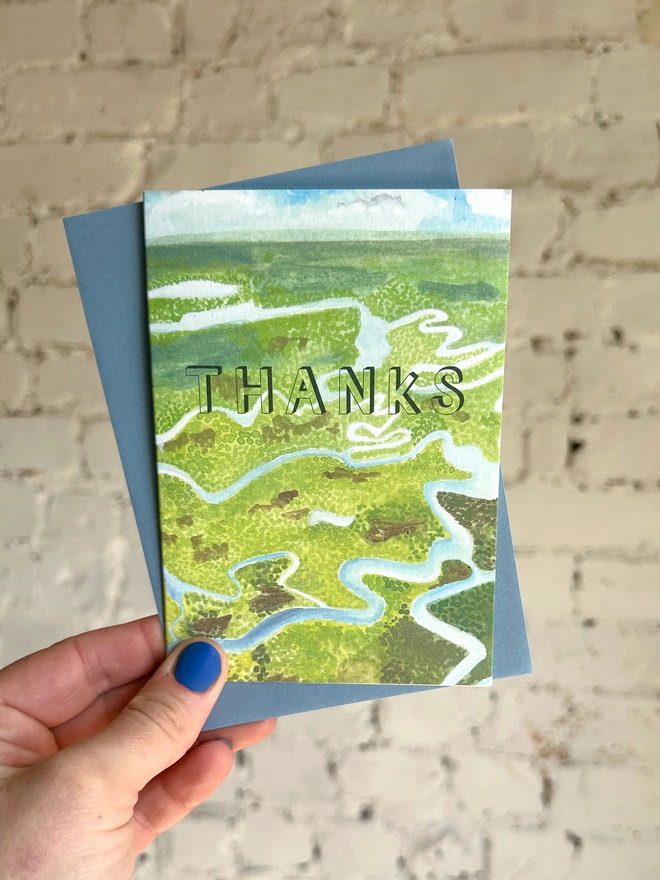 a greetings card featuring an illustration of the everglades landscape with the text “thanks” with a blue envelope