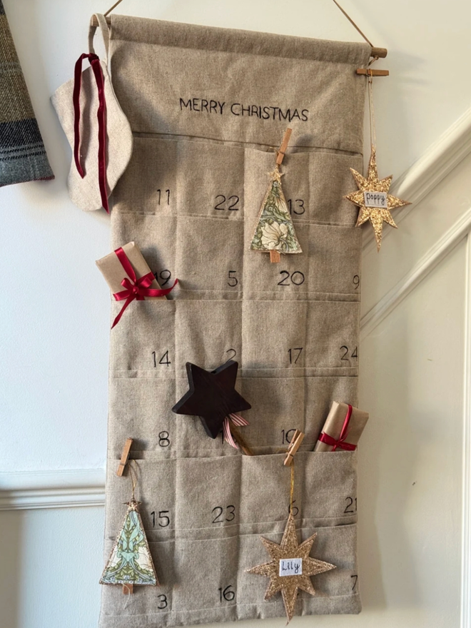 Linen Embroidered Advent Calendar. An advent calendar hanging on a wall, filled with Christmas treats.