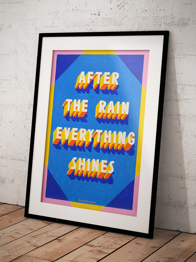 Art print of painted 3d typography reading After The Rain Everything Shines in a black frame leaning against a wall