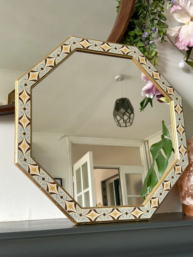 Medium sized octagonal wall mirror with a hand painted decorated frame with gold stars and blue star burst repeating pattern around the frame