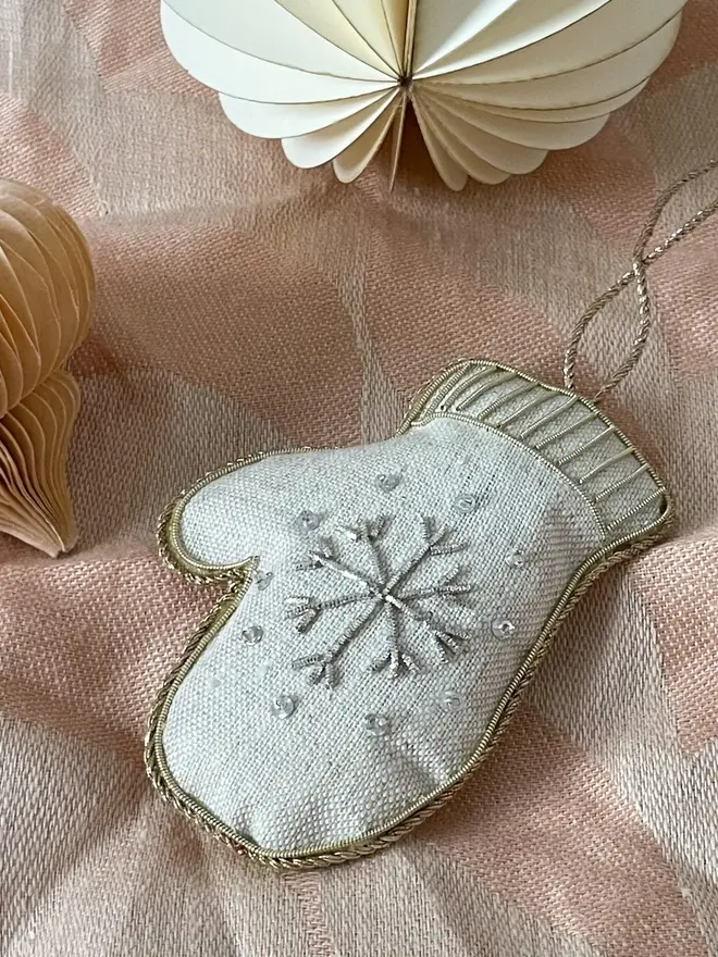 embroidered linen mitten decoration. pale mitten hanging ornament embroidered with snowflake photographed against pink fabric.