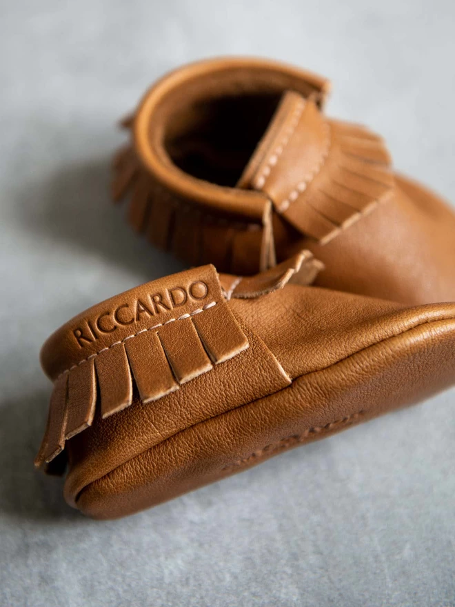 Plain embossed personalised monogram detailing on the ankle of Amy and Ivor baby moccasins in classic tan