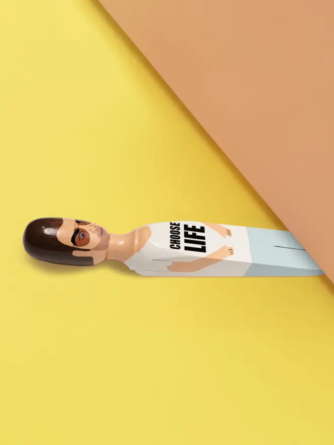 Wooden Door Stopper (Georg Choose Life Outfit), a colourful wooden door stop sitting under a door.