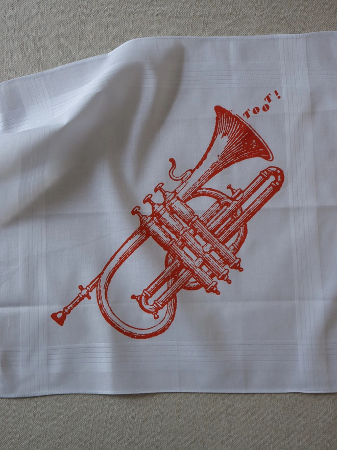 A Mr.PS Toot trumpet map hankie printed in orange laid flat on a linen tablecloth
