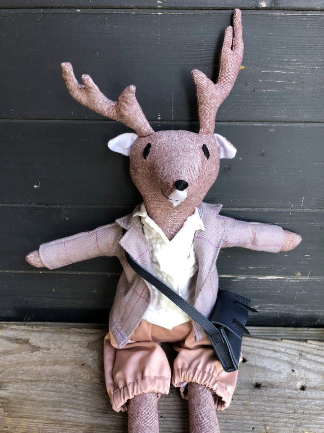 Soft toy reindeer,wearing lilac tweed jacket,white shirt, pink shorts and blue leather satchel