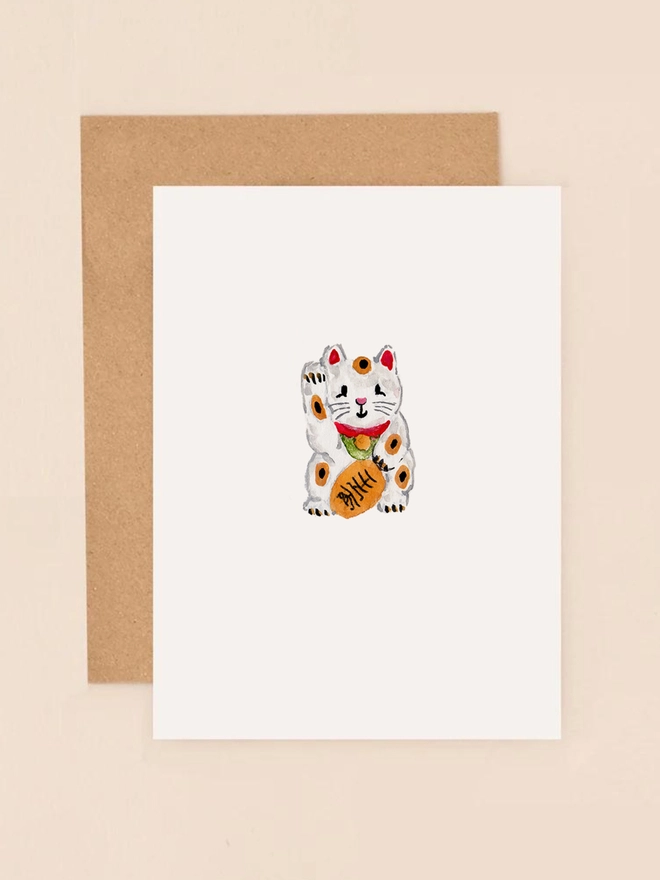A charming illustration of a traditional Japanese Maneki-neko, or lucky cat, with its paw raised in a welcoming gesture. The cat is adorned in a vibrant red collar with a golden bell, set against a soft, pastel background. The design exudes warmth and positivity, symbolising good fortune and prosperity.