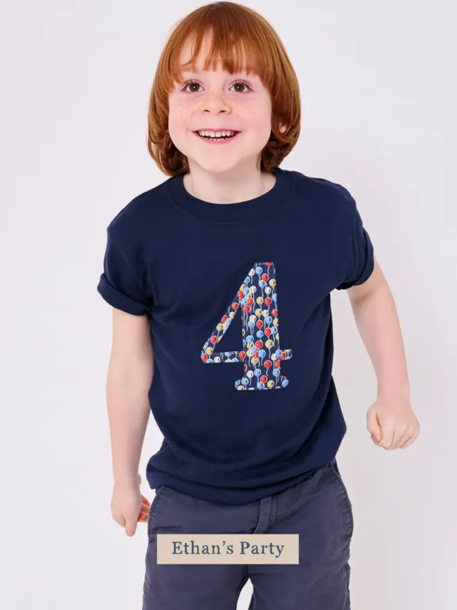a 4 year old boy wearing a navy birthday t-shirt with a number 4 cut from liberty balloon print on the front