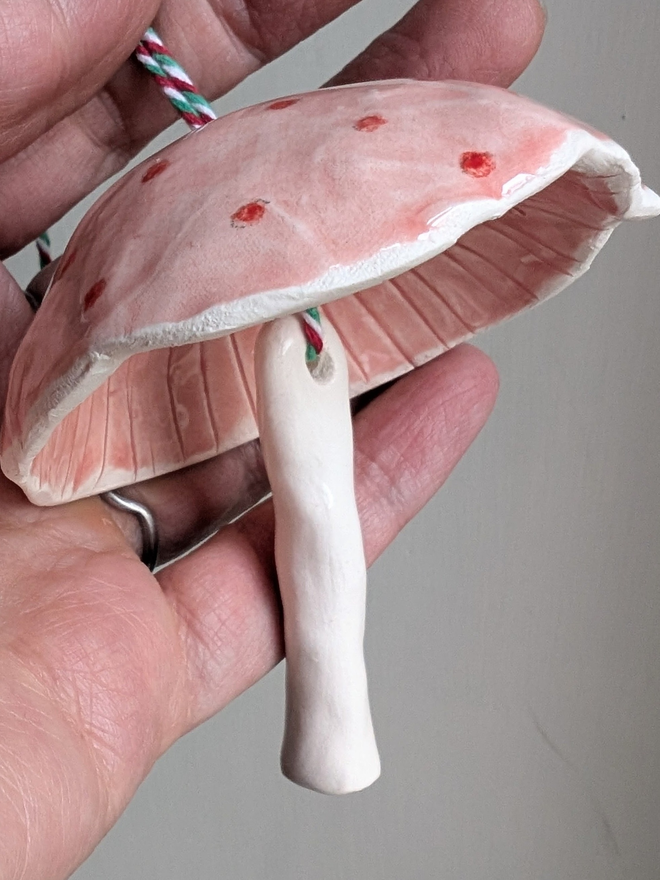 pink and red spotty ceramic mushroom hanging bell decoration held in a hand against a pale grey background