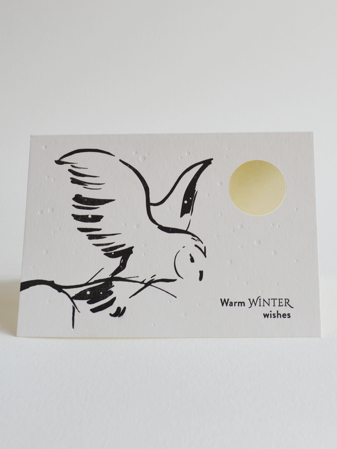 Simple black and white illustrated greeting card with snowy owl and cut-out moon feature.  Words say warm winter wishes.