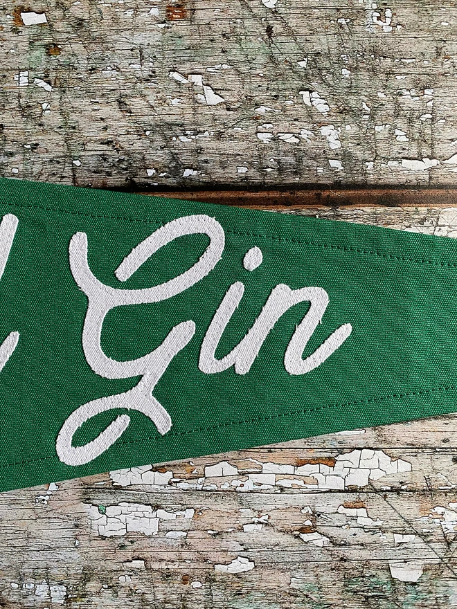 A close up of the word Gin written in ivory canvas. Detail of a green Coffee before Gin pennant flag