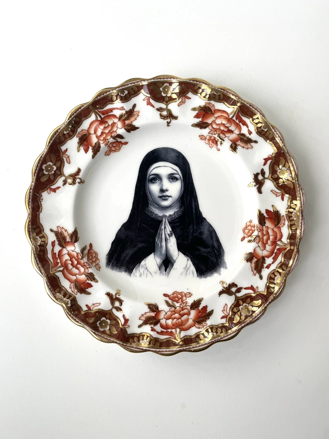 a vintage plate with an ornate frame, and within the centre is a vintage illustration of pretty nun praying