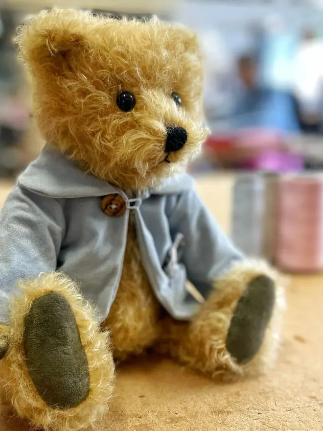 Handmade teddy bear with soft textured fur, wearing a blue jacket, posed against a plain background.
