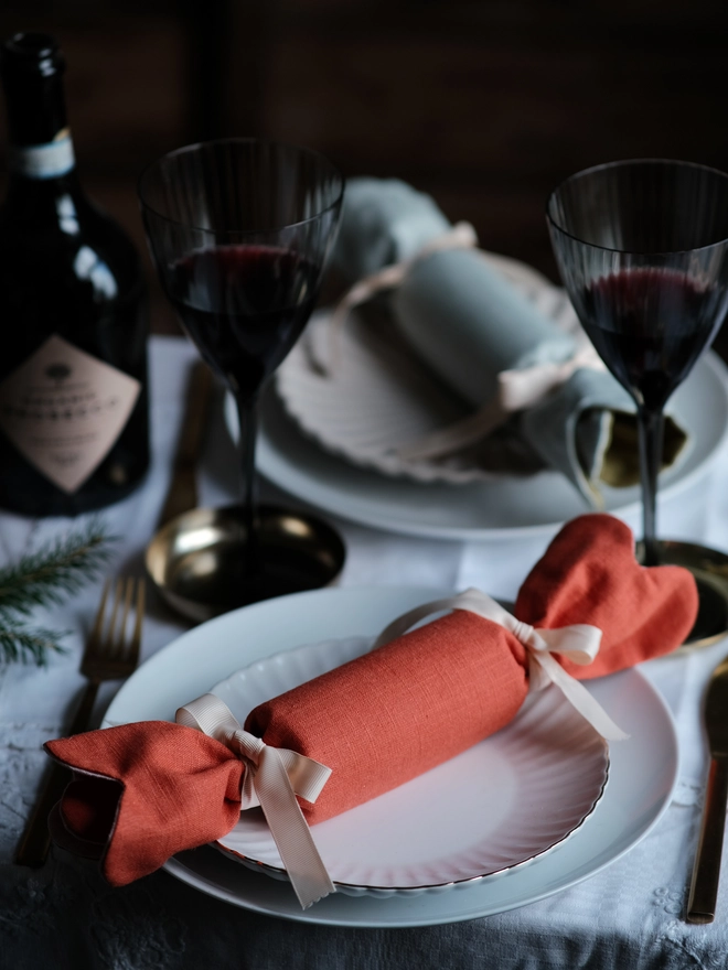 Reversible reusable linen Christmas crackers in soft pink, sage green, cream and muted festive colours, tied with natural ribbon and arranged on a family Christmas table