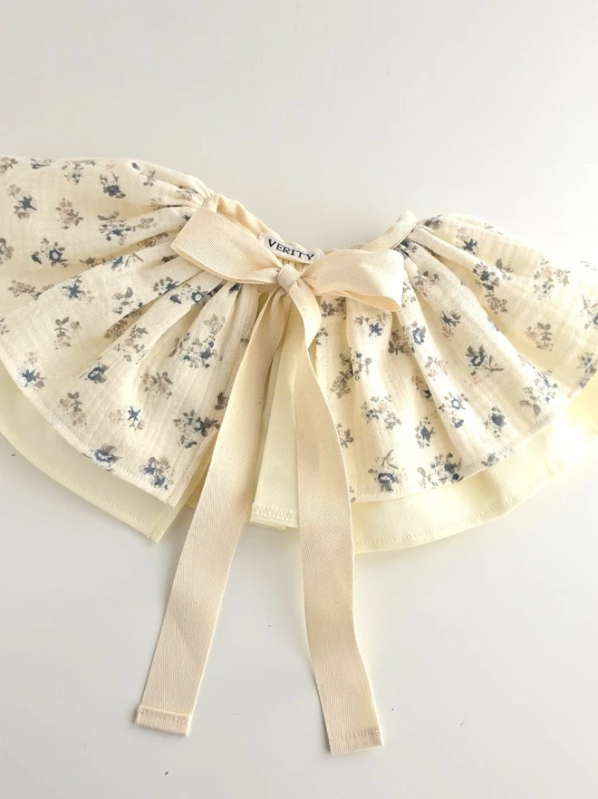 Handmade Mabel floral birthday cape in soft vanilla cotton double gauze with delicate blue ditsy floral print, cotton lining and natural twill ribbon ties.