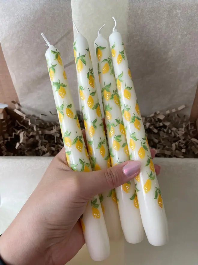 Lemon Zesty & Orange Bloom Hand Painted Candles, a woman holding a group of lemon and orange taper candles in her hand above a floor. 