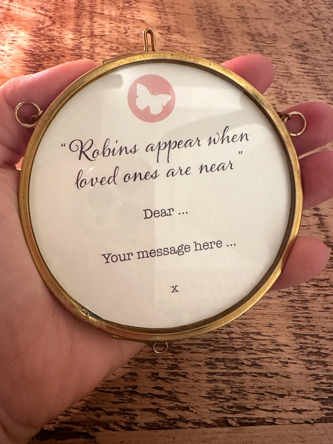 A photo showing the message 'Robins appear, when love ones are near" on the back of the circular, brass, hanging frame, with option to add personalised message.
