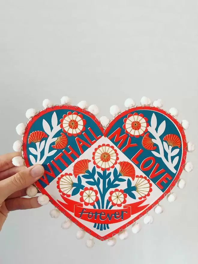 Fiona's hand holds a colourful wooden valentine heart which reads 'With all my love, forever’