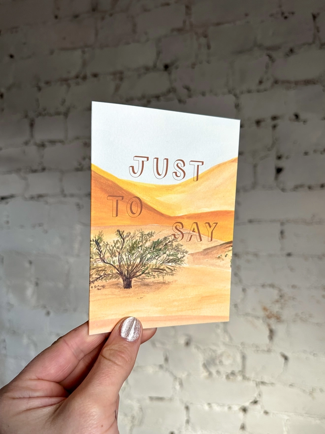 a greetings card featuring an illustration of a desert landscape with the text “just to say”