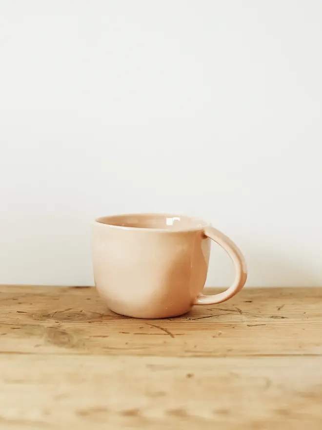 handcrafted stoneware mug. a pink stoneware mug on a wooden bench.