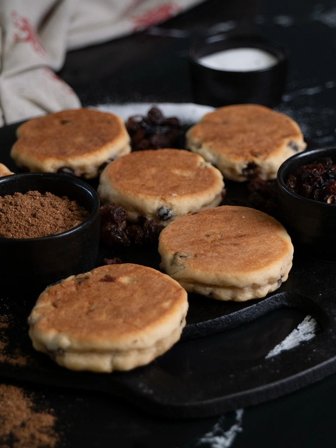 Traditional Welsh Cakes on a griddle/bakestone with ingredients in ramekins