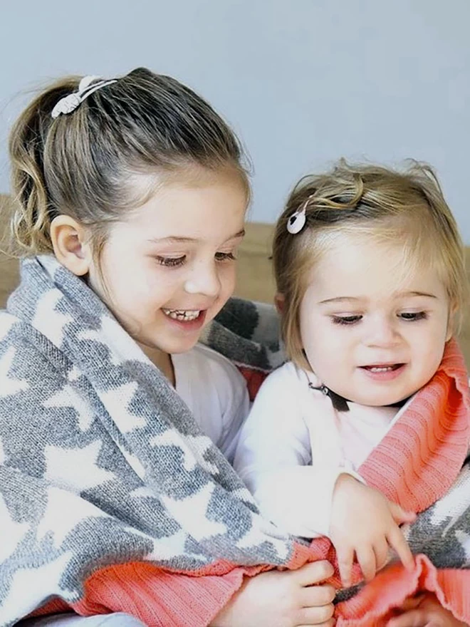 Two smiling girls sitting cuddled together with a grey and white star blanket wrapped around their shoulders.