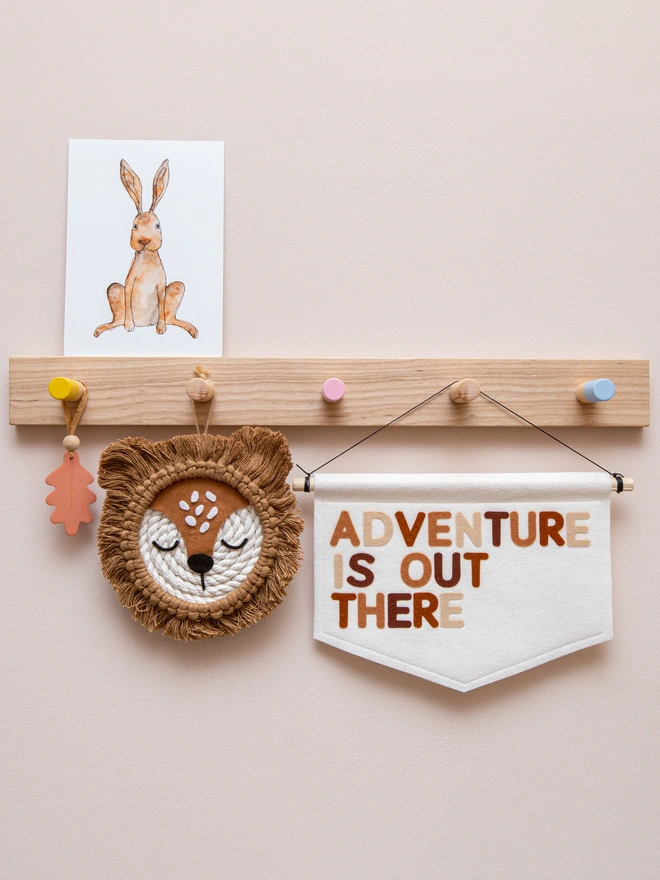 White felt banner with the words "Adventure is out there" written on it in a mix a brown, neutral themed colours