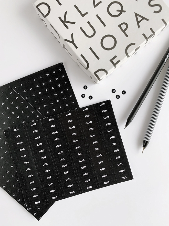 Close up of the Undated Diary Dots Sticker Pack, a black HELLO TIME pencil and a fine liner. 