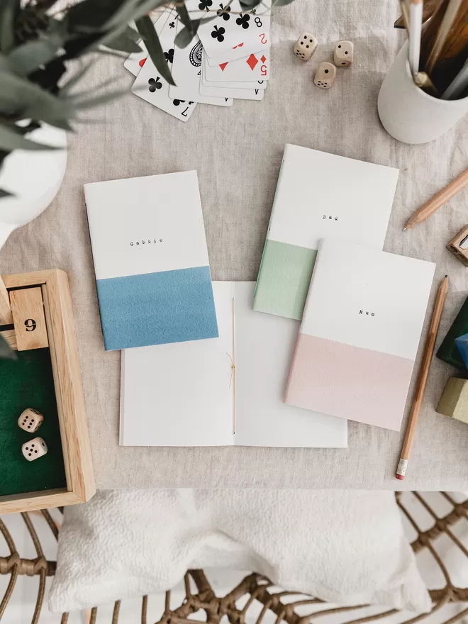 one notebook open showing the hand stitched middle pages the three other notebooks closed are pink, green and blue