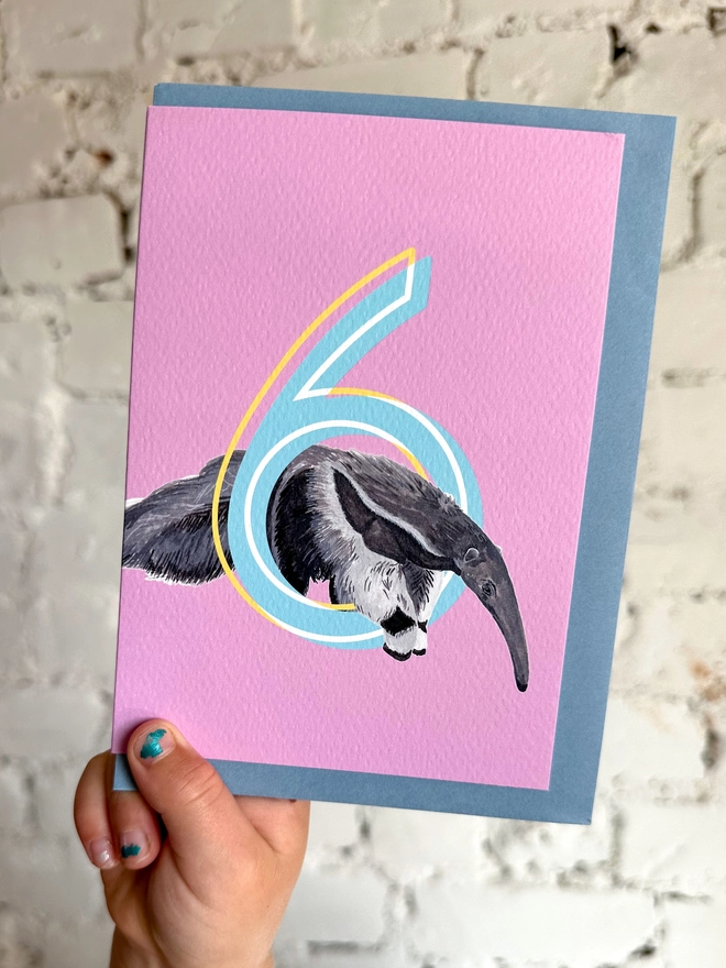a pink card featuring a big blue number 6 and a giant anteater illustration with a blue envelope