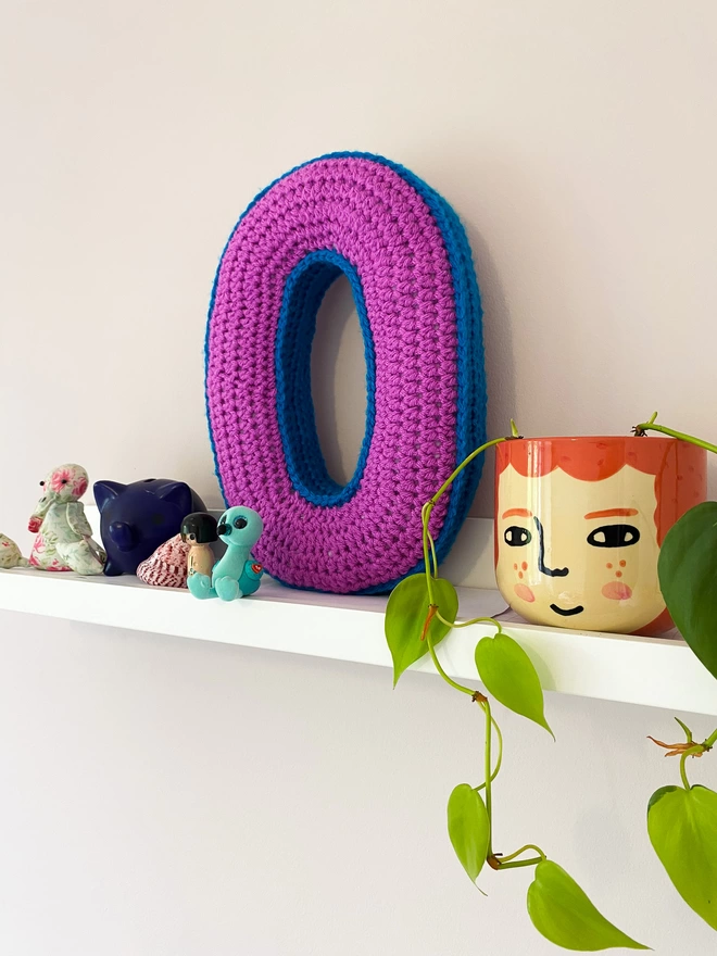 O Shaped Cushion in Magenta and Blue, on a child's shelf
