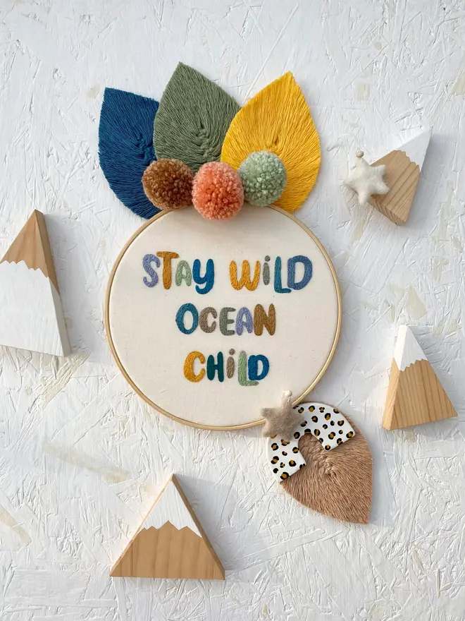 custom phrase embroidered hoop. cotton hoop embroidered with 'stay wild ocean child' in colourful lettering.