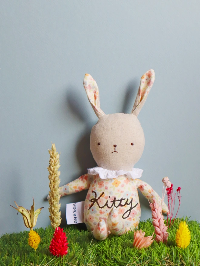 Handmade rabbit doll made from pastel floral fabric, with a stitched face, long ears, ruffled white collar.