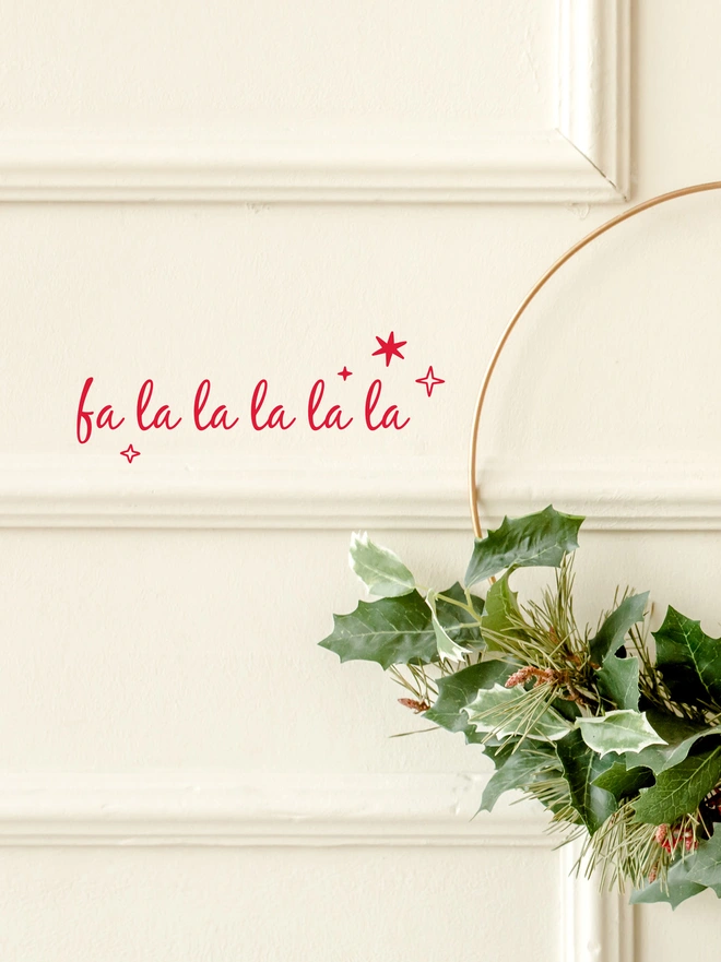 white wall with panelling and a red sign which says Fa La La La La La, there are two stars above and one below