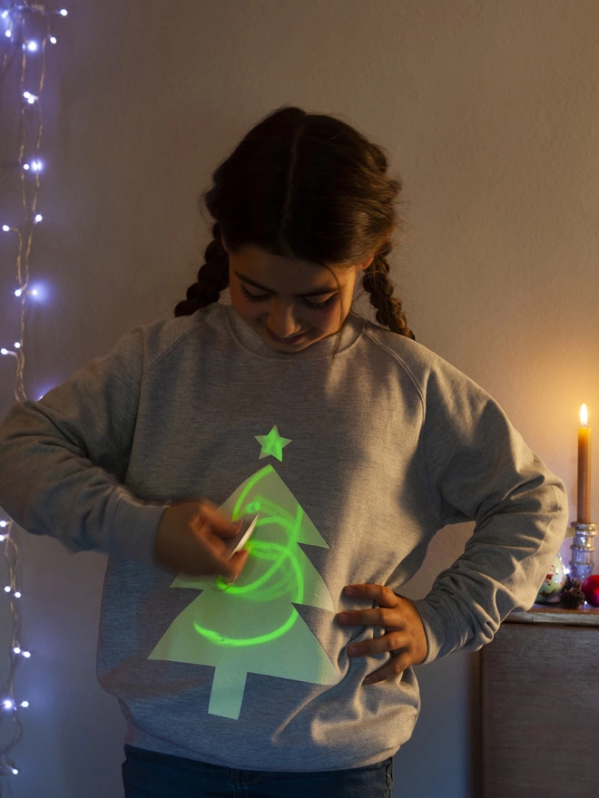 Girl drawing with penlight onto a glow in the dark xmas jumper with tree printed on it