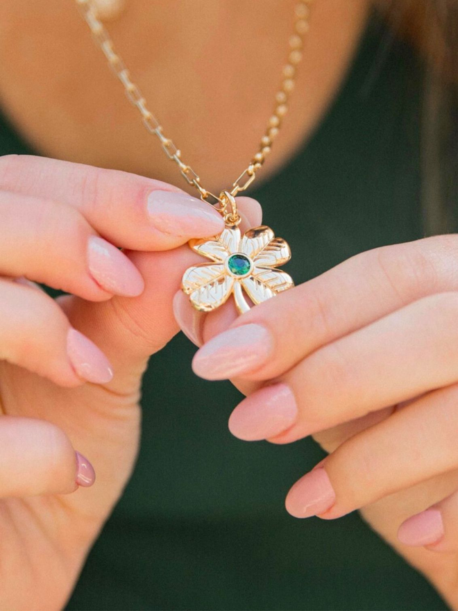 Women's hands holding a gold and green stone lucky clover charm