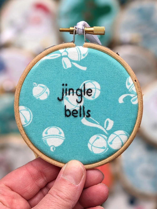 A hand embroidered hoop on Christmas fabric reading jingle bells