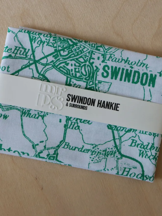 A folded Mr.PS Swindon map hankie printed in green, on a wooden table