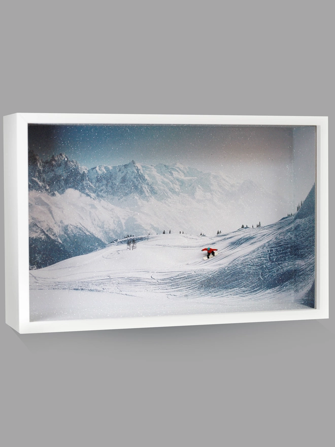 Miniature scene in an artbox showing a tiny snowboarder cruising down a snowy mountainface
