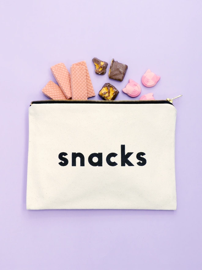a natural canvas zip pouch with the words snacks with biscuits and sweets spilling out 