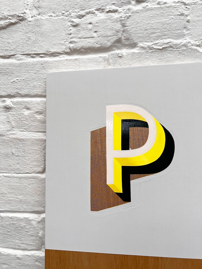 Close up of letter P from PLAY hand painted sign in neon yellow, lilac and grey, against a white brick wall, straight on. 