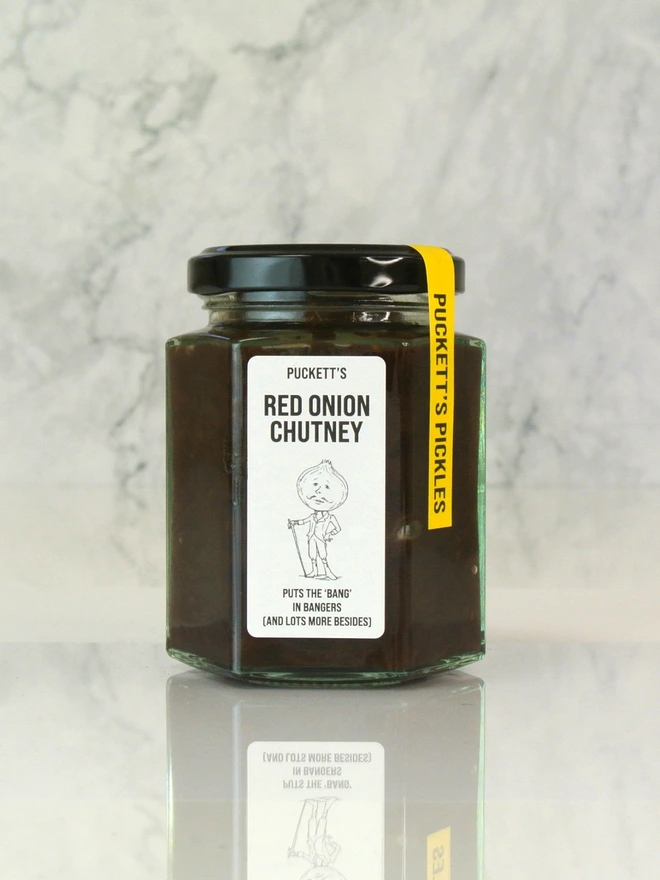 red onion chutney. a jar of chutney photographed against a marble background. 