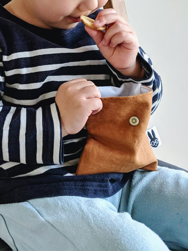 reusable linen snack pouch. a child holding rust brown pouch and eating snacks.