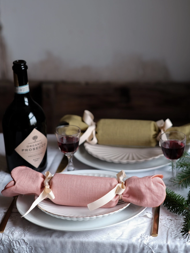 Reversible reusable linen Christmas crackers in soft pink, sage green, cream and muted festive colours, tied with natural ribbon and arranged on a family Christmas table