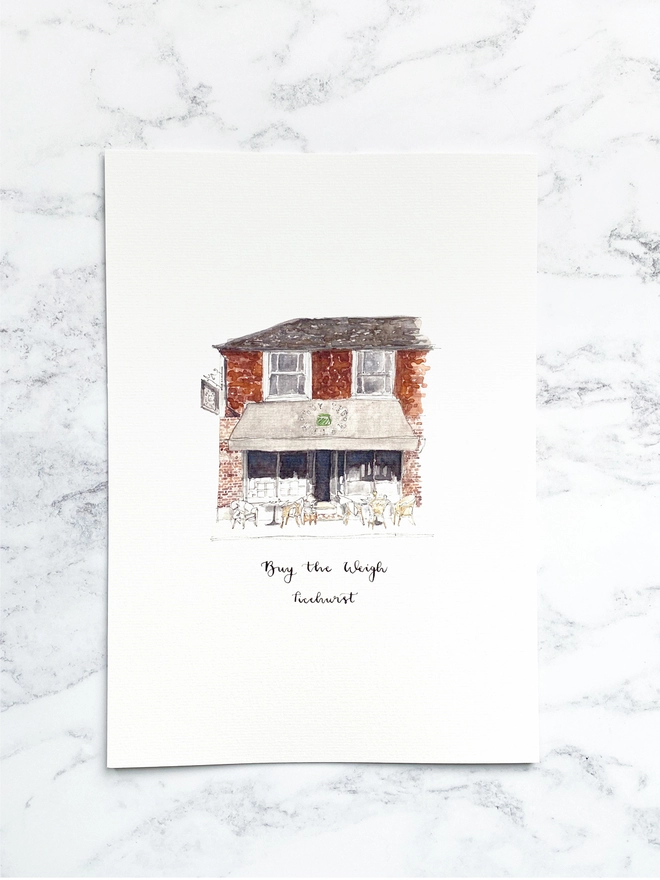 Watercolour painting of Buy the Weigh, zero wase shop in Ticehurst, a beautiful brick building with a teracotta tile on the first floor, white sash windows and a grey awning. The watercolour style is painted with a black pen outline and organic loose style with small details. The print is on A4 white paper and sits on a white marble background. 