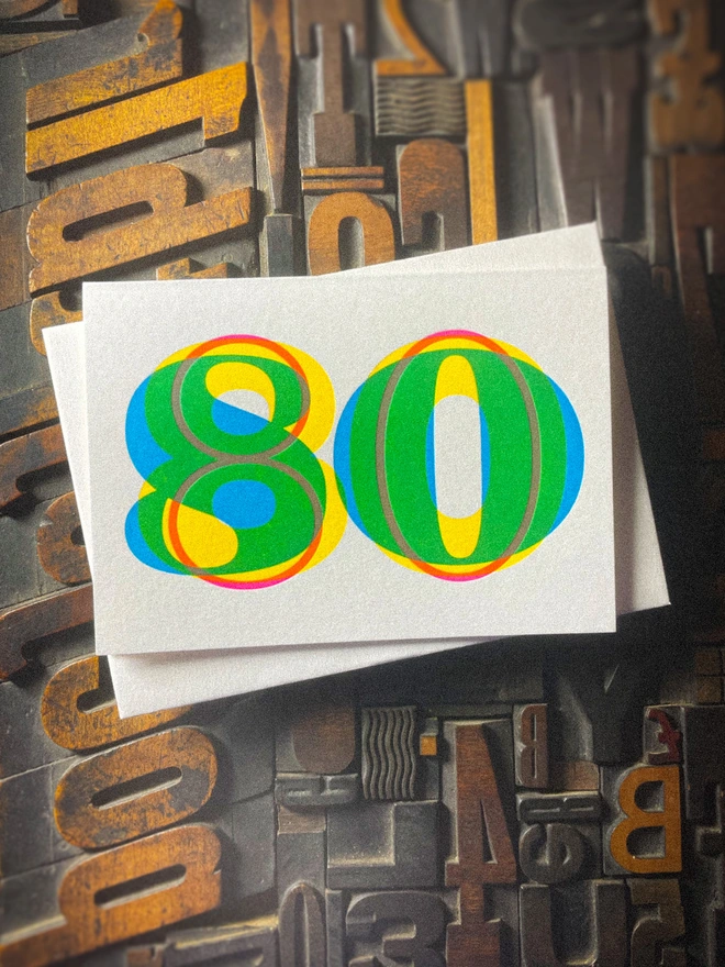 Handmade letterpress 80th birthday card featuring bold overlapping numerals printed in vibrant fluorescent cyan, magenta and yellow inks. Each card is individually hand printed using traditional letterpress techniques on luxury paper stock, creating a beautifully tactile finish with a subtle deboss and rich layered colours inspired by the CMYK printing process.