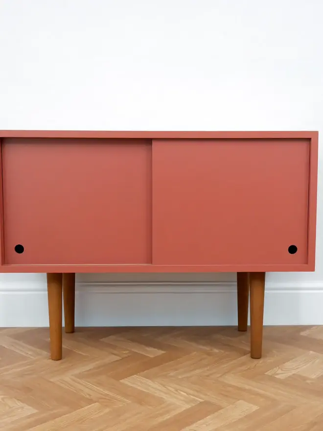 Mid-century cabinet with coral sliding doors and wooden tapered legs.