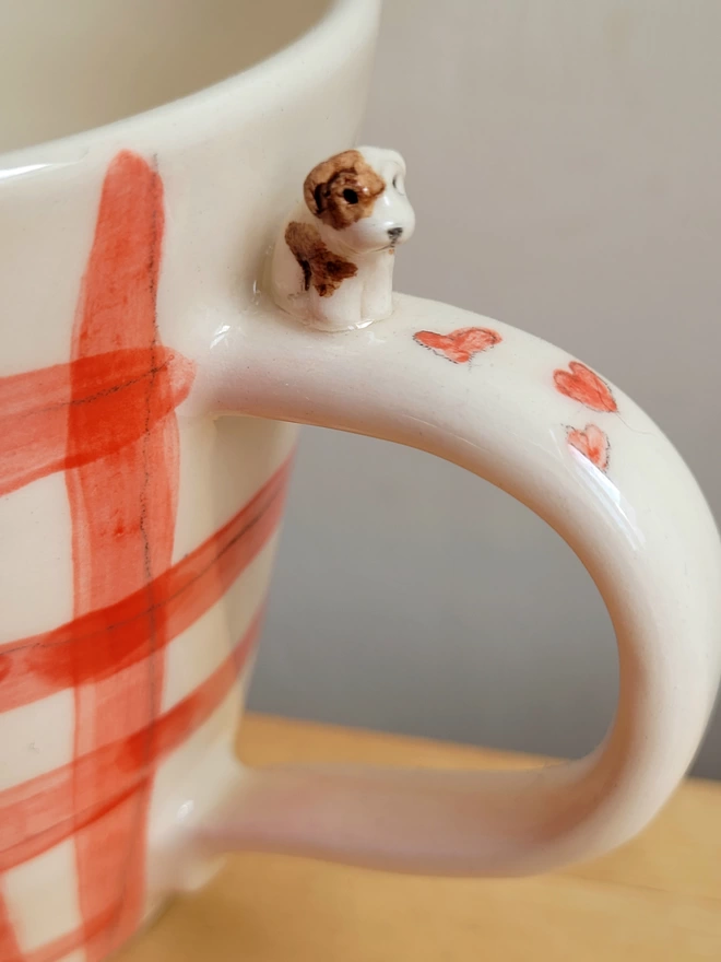 close up of a red gingham cup with red heart and miniature brown and white dog on the handle 